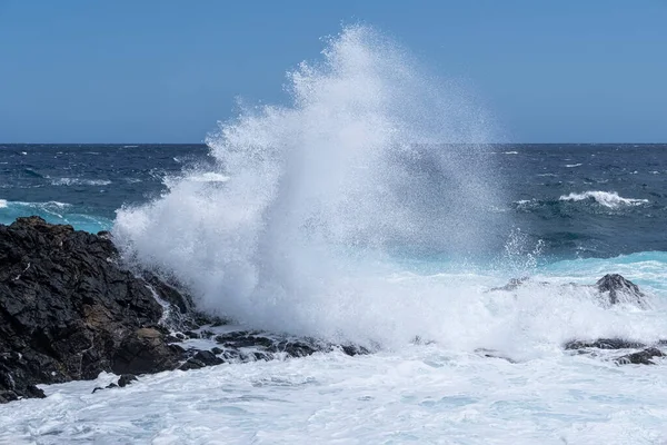 a big wave breaks against some rocks on the seashore, on a rough sea day, foam from the waves on the blue ocean, powerful splash of waves breaking against the sharp rocks