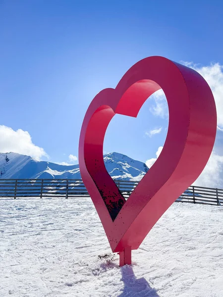 a big red metal heart in the middle of a ski slope, with snowy mountains, passion for skiing, winter sport, valentines day, copy space, vertical