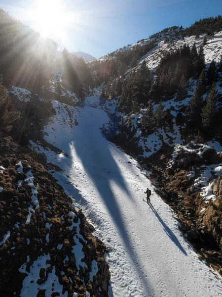 a backcountry skier climbs up a mountain pass on his way to the summit, projecting a long shadow behind him, the sun rises behind the mountains, vertical