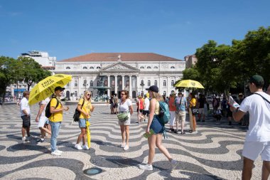 a group of tourists looking for a free tour guide with a yellow umbrella, at Rossio Square in Lisbon, Portugal