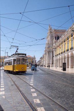 lisbon commerce square with a typical yellow streetcar and a blue tuc tuc, tourists in the background visiting the square in the Baixa district, vertical