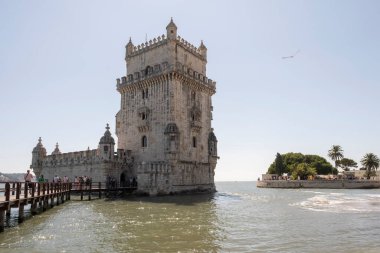Belem defensive tower in the estuary of the Tagus river in Lisbon, tourists walk along the footbridge over the water that leads to the interior, horizontal
