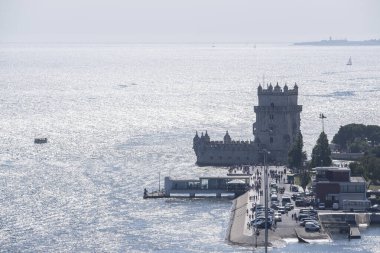 aerial image of the Tagus river estuary in Belem, Lisbon, boats on the river, distant people visiting the tower of Belem backlight, horizontal