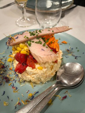 delicious plate with russian salad, red peppers, corn and a piece of tuna belly on top in a plate decorated with edible flowers, vertical
