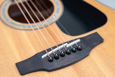 detail of the bridge of a light wood acoustic guitar with its saddle and pins, selective focus, horizontal