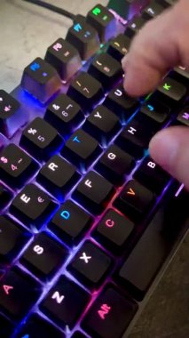 Çalan bilgisayarın klavyesinin tuşlarına basan bir eli kapat, arka planda siyah tuşlar renk değiştirsin, insan eli klavyeye dokunsun, RGB ışığı, 4k, dikey