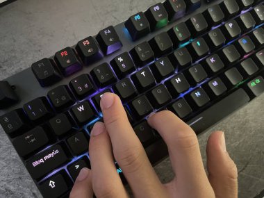 Çalan bilgisayarın klavyesinin tuşlarına basan bir eli kapat, arka planda siyah tuşlar renk değiştirsin, insan eli klavyeye dokunsun, RGB ışığı, yatay