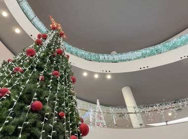 Bir alışveriş merkezinin içindeki büyük bir noel ağacı perspektiften bakıldığında, kırmızı toplarla süslenmiş ve tepesinde büyük bir yıldız, noel alışverişi, yatay