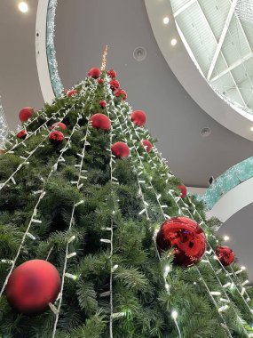 Bir alışveriş merkezinin içindeki büyük bir noel ağacı perspektiften bakıldığında, kırmızı toplarla süslenmiş ve en tepede büyük bir yıldız, noel alışverişi, dikey