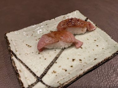 Kahverengi deri bir hasırın üzerinde seramik bir tabakta flambe balık niguiri, flambe balıklı lezzetli niguiri, tipik Japon yemeği, Japon restoranı, iki kişilik yemek, yatay