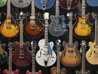 Farklı renklerde elektro gitarlarla dolu siyah bir duvar, yarı boş ve boş stil, gitarlar sergi salonu, yatay