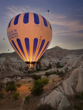 Sıcak hava balonu, Cappadocia 'da şafak vakti peri bacası arasında yer seviyesinde uçar. Kullan at telefonun parıltısı balonu ve zemini dikey olarak aydınlatır.