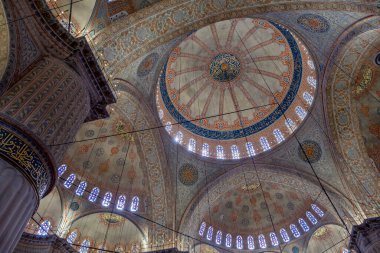 İstanbul 'daki mavi caminin içi, renkli vitray pencereleri, geniş kemerleri, etkileyici tavanı, merkez mahzeni ve ön planda büyük sütunuyla Sultan Ahmed Camii.