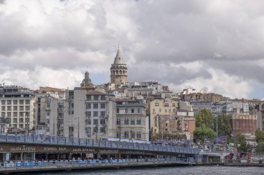 Galata Köprüsü 'nün altında ünlü balık lokantası arka planda bulutlu gökyüzüne karşı uzanan Galata Kulesi.