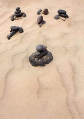 sakin kumlu bir plajda dizilmiş yuvarlak taşlar, kumdaki rüzgarın oluşturduğu yumuşak doğal desenler, denge, uyum, kopya alanı, plaj dokusu, dikey konsepti temsil ediyor.