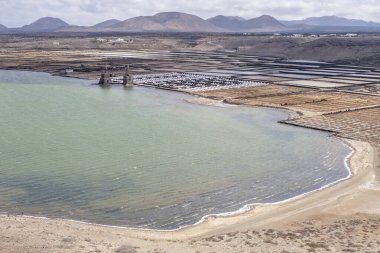 Deniz kenarındaki bir körfezdeki deniz tuzu tavasının hava görüntüsü, arka planda volkanik bir manzara, Janubio tuz tavası, Lanzarote, Kanarya Adaları, İspanya, yatay