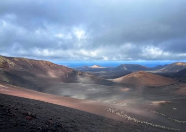 Önünde bir volkanik krater olan volkanik manzara ve bulutlu bir günde arka planda okyanus, Timanfaya Ulusal Parkı, Lanzarote, Kanarya Adası, İspanya