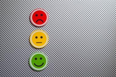 Kırmızı, sarı ve yeşil renkte üç yuvarlak emoji yüz, metalik dokulu bir arka planda hüzünlü, nötr ve mutlu duyguları temsil ediyor, geri bildirim veya ruh halini sembolize ediyor, kopyalama alanı, yatay