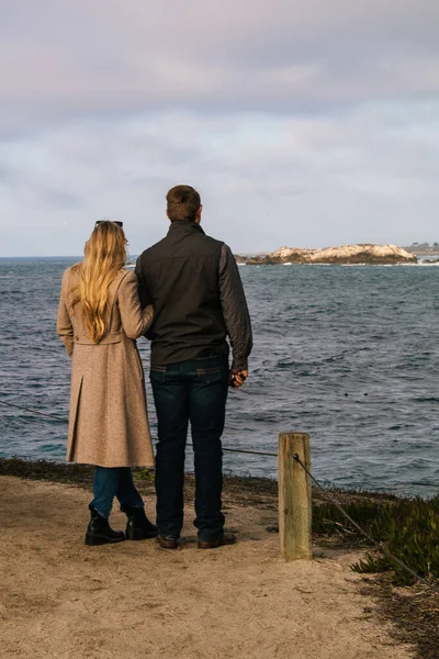 Two People Stand on the Coastline of 17-Mile Drive, Carmel California, watching the Pacific Ocean's Waves Rise and Fall just before Sunset