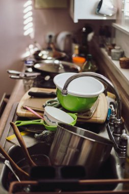 A counter and sink is filled to the brim with dirty dishes. The kitchen is cluttered with bowls, pans, and utensils that need washing. A pile of mess.