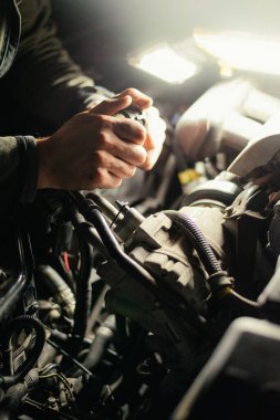 Man works on a car engine replacing hose for coolant. Mechanic fixes a vehicle at night. 