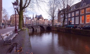 Gün batımında şehrin seddini ve ortaçağ peri evlerinin cephelerini gösteren resimli bir manzara. Amsterdam mı? Hollanda.