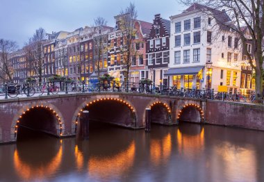 Gün batımında şehrin seddini ve ortaçağ peri evlerinin cephelerini gösteren resimli bir manzara. Amsterdam mı? Hollanda.