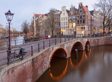 Gün batımında şehrin seddini ve ortaçağ peri evlerinin cephelerini gösteren resimli bir manzara. Amsterdam mı? Hollanda.