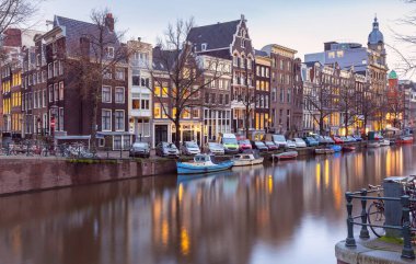 Gün batımında şehrin seddini ve ortaçağ peri evlerinin cephelerini gösteren resimli bir manzara. Amsterdam mı? Hollanda.
