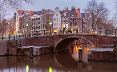 Gün batımında şehrin seddini ve ortaçağ peri evlerinin cephelerini gösteren resimli bir manzara. Amsterdam mı? Hollanda.