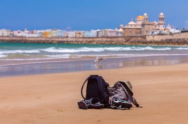 İki sırt çantası, bir şapka ve bir sandalet denizin arka planında kumlu bir plajda yatıyor. Cadiz. İspanya.