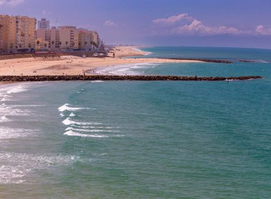 Güneşli bir günde kumlu bir plajın ve mavi denizin arkaplanına bakan Cadiz manzarası.