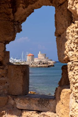 Rodos adasındaki eski bir taş kale duvarından yel değirmenleri ve deniz feneri manzarası. Yunanistan.