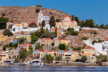 Güneşli bir günde, bir körfezin kıyısındaki Yunan köyü Symi 'de renkli geleneksel evler. Yunanistan.