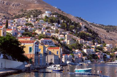 Güneşli bir günde, bir körfezin kıyısındaki Yunan köyü Symi 'de renkli geleneksel evler. Yunanistan.