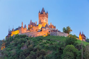 Ortaçağ Avrupa kalesi Reichsburg 'da gün batımında bir tepede gece aydınlanması. Cochem, Almanya.