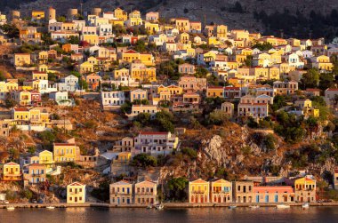 Gün batımında, Suriye adasındaki dik yamaçlardaki renkli geleneksel evlerin manzarası. Yunanistan.