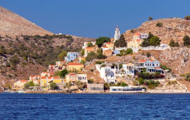 Güneşli bir günde, körfezin kıyısındaki Yunan köyü Symi 'de renkli geleneksel evler ve balıkçı tekneleri. Yunanistan.