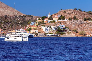 Güneşli bir günde, körfezin kıyısındaki Yunan köyü Symi 'de renkli geleneksel evler ve balıkçı tekneleri. Yunanistan.