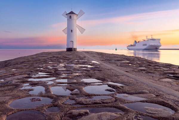 Сценический вид старого каменного маяка в виде ветряной мельницы на волнорезе на рассвете. Swinoujscie. Померания. Польша.