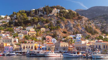 Güneşli bir günde, Symi balıkçı köyündeki renkli geleneksel evler ve balıkçı tekneleri manzarası. Yunanistan. Dodekanca.