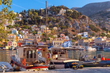 Güneşli bir günde, Symi balıkçı köyündeki renkli geleneksel evler ve balıkçı tekneleri manzarası. Yunanistan. Dodekanca.