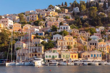 Güneşli bir günde, Symi balıkçı köyündeki renkli geleneksel evler ve balıkçı tekneleri manzarası. Yunanistan. Dodekanca.