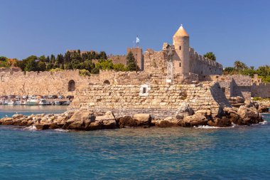 Güneşli bir günde mavi parlak denizin arka planına karşı eski kalenin duvarlarını ve kulelerini görmek. Rodos. Yunanistan.