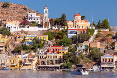 Güneşli bir günde, balıkçı köyü Symi 'de renkli geleneksel evler ve balıkçı tekneleri görülüyor. Yunanistan. Dodekanca.