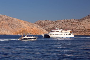 Dağların arka planında mavi bir körfezde turist gemileri. Symi. Yunanistan.