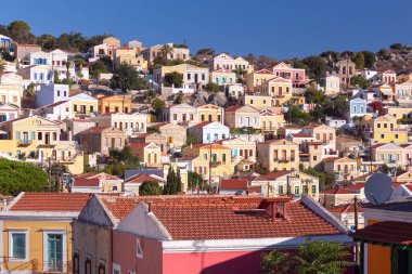 Balıkçı köyü Symi 'nin körfezindeki renkli geleneksel evler ve balıkçı tekneleri güneşli bir günde, Yunanistan, Dodecanese.