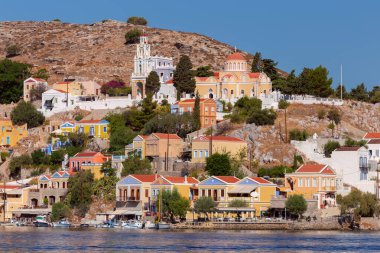 Balıkçı köyü Symi 'nin körfezindeki renkli geleneksel evler ve balıkçı tekneleri güneşli bir günde, Yunanistan, Dodecanese.