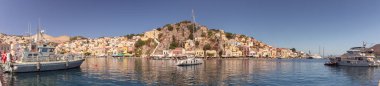 Güneşli bir günde, Suriye köyünde renkli geleneksel evler ve balıkçı teknelerinin panoramik manzarası, Yunanistan ve Dodecanese.