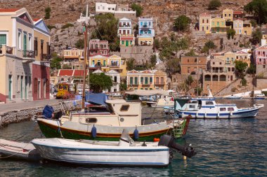 Güneşli bir günde, Yunanistan 'ın Dodecanese kasabasında renkli geleneksel evler ve balıkçı tekneleri görülüyor